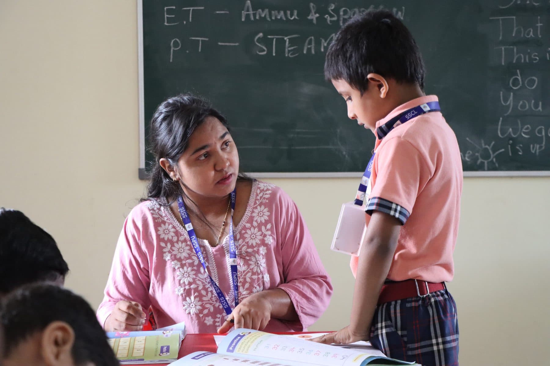 A teacher guiding a boy through his book by the blackboard
