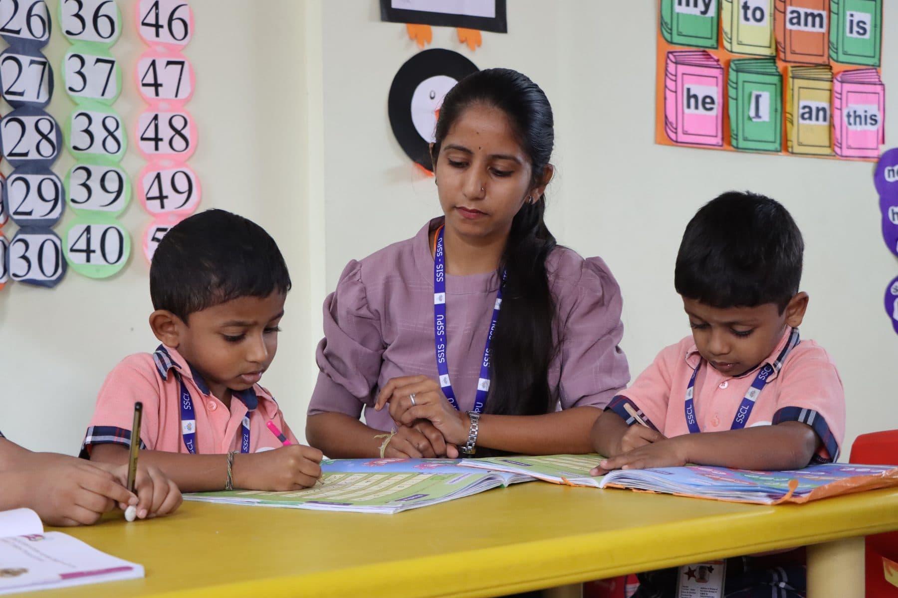 A teacher helping two boys with their writing at a yellow table