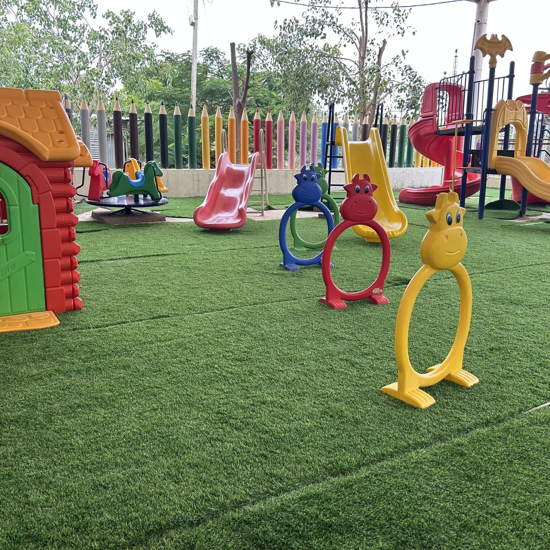 Yellow climbing hoops, slides and a little play house on green turf