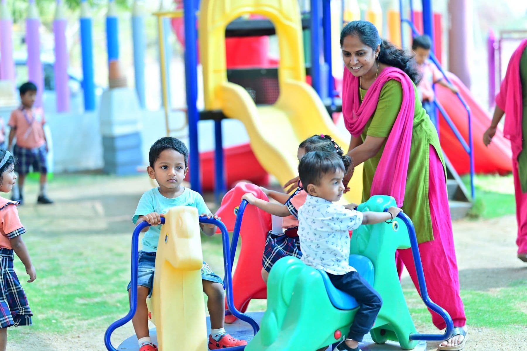 Toddlers on rocking toys in the play garden with their teacher