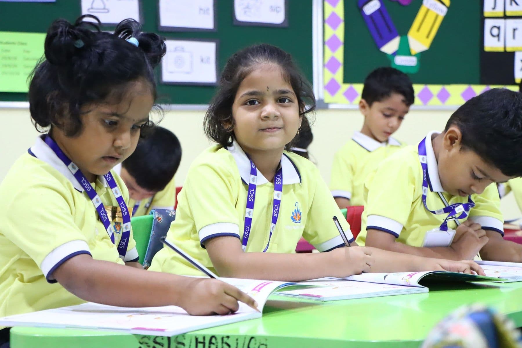 A girl writing in her book while she smiles at the camera
