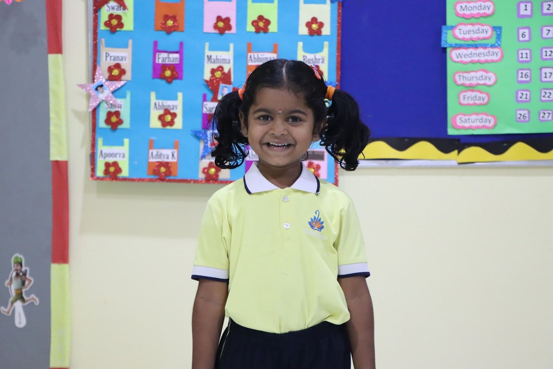 A proud little girl standing in front of a colourful classroom display