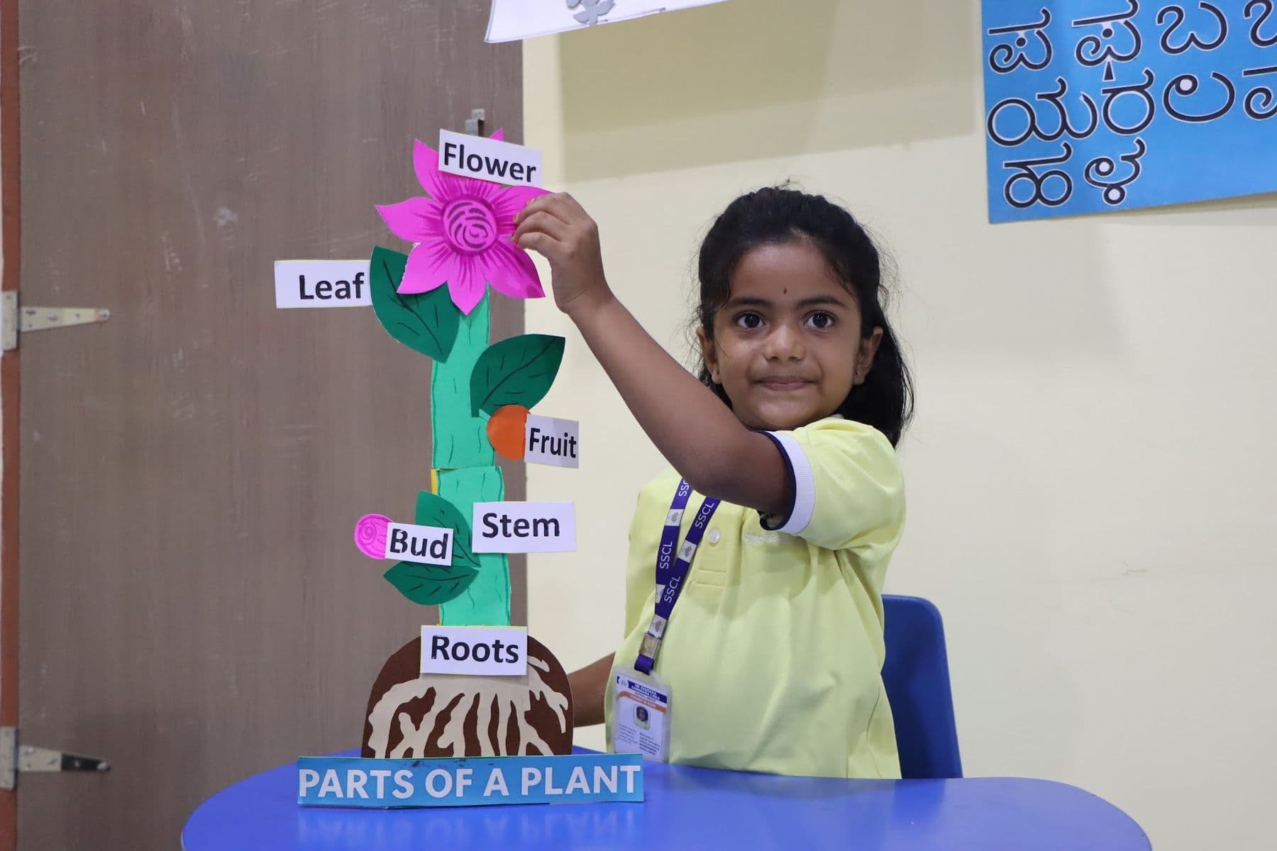 A smiling girl pointing at the flower on her plant model