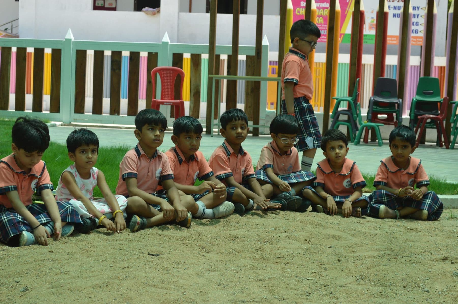 A row of children sitting on the sand, listening