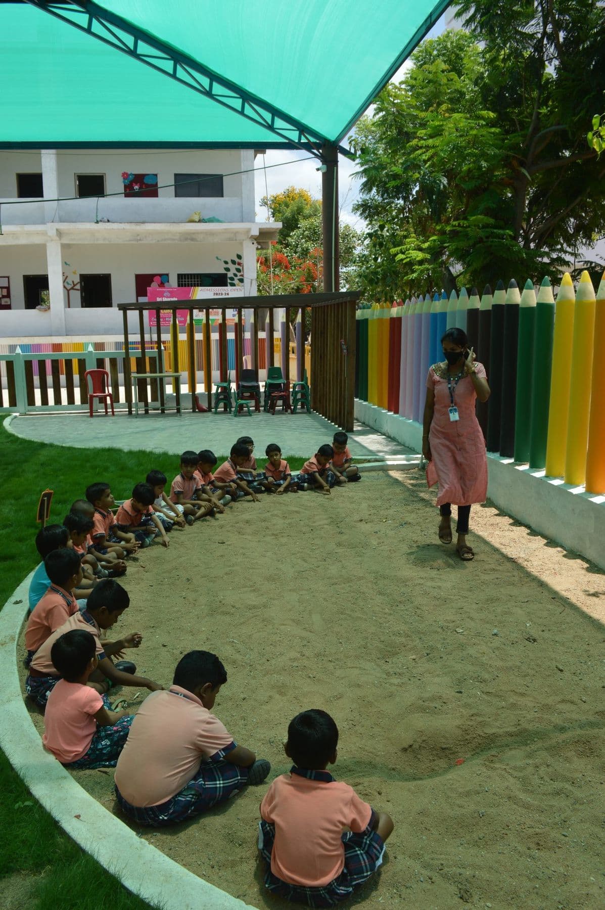Children sitting in a circle in the garden with their teacher