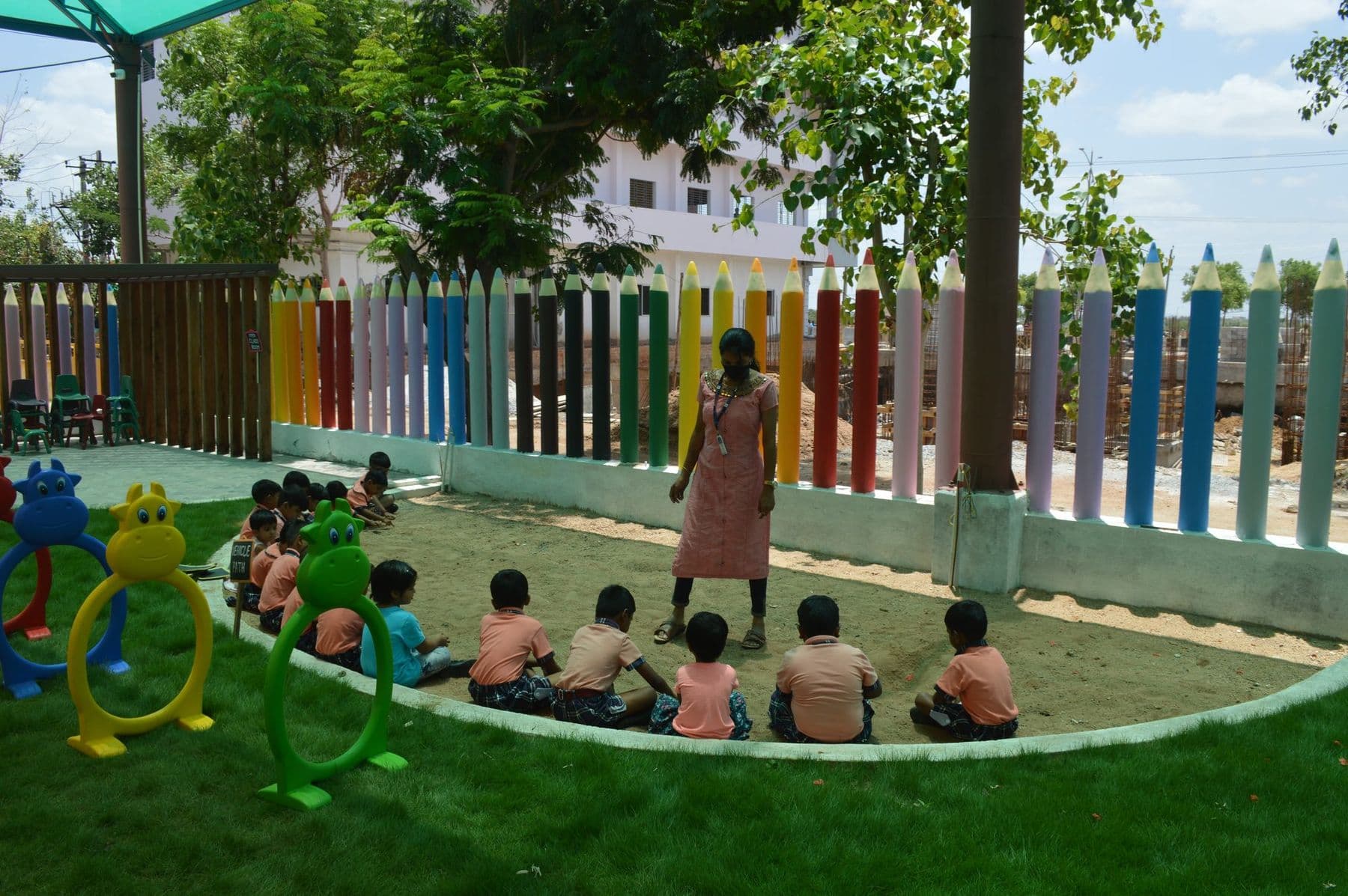 Children in a circle on the lawn beside the pencil fence