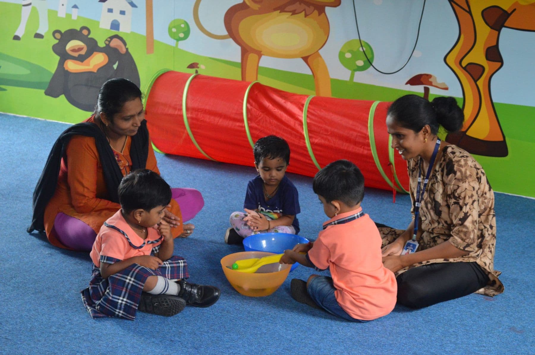 Toddlers playing with bowls and a play tunnel with their teachers
