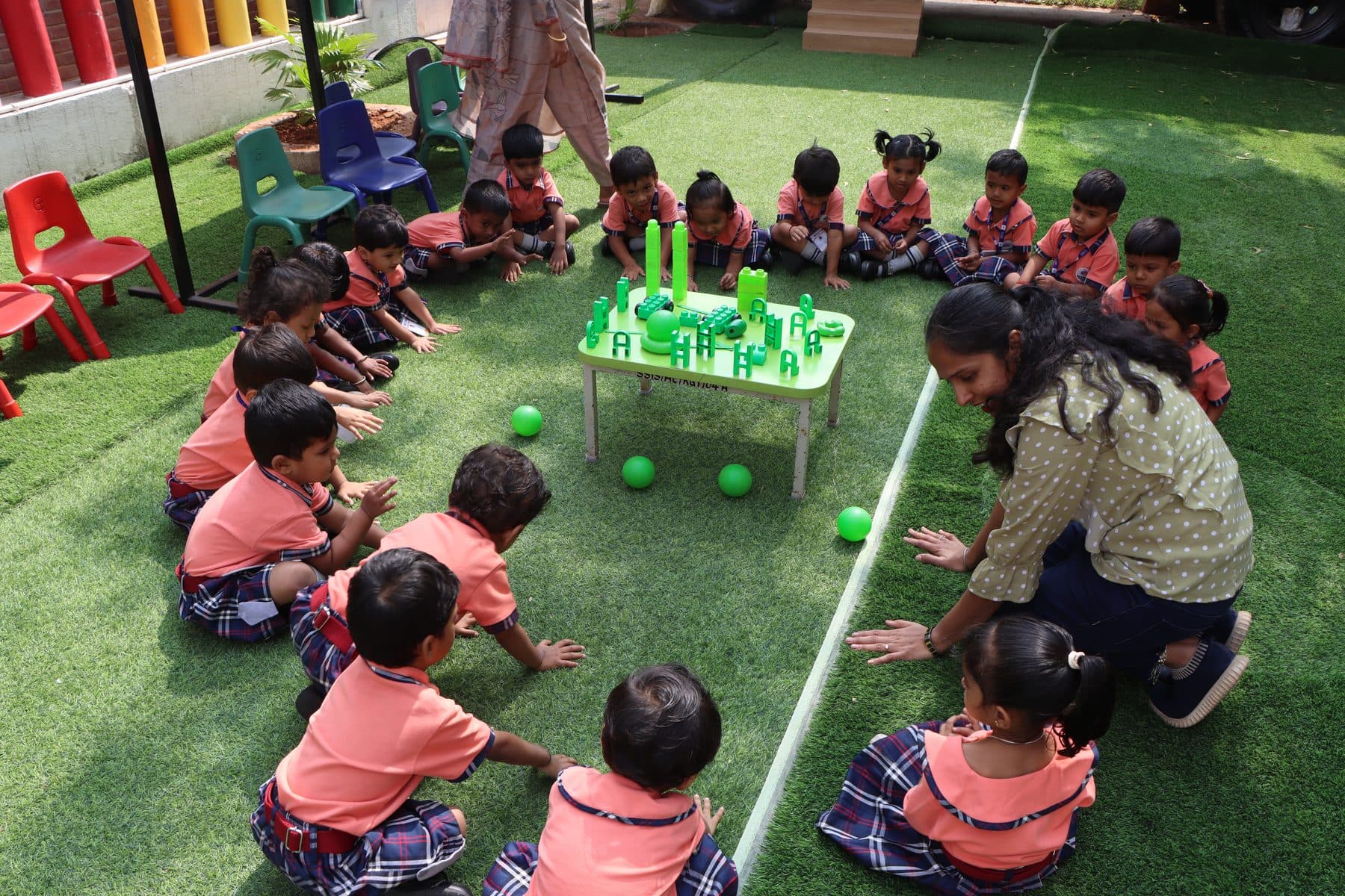 A teacher leading a ball game for children sitting in a circle on the grass