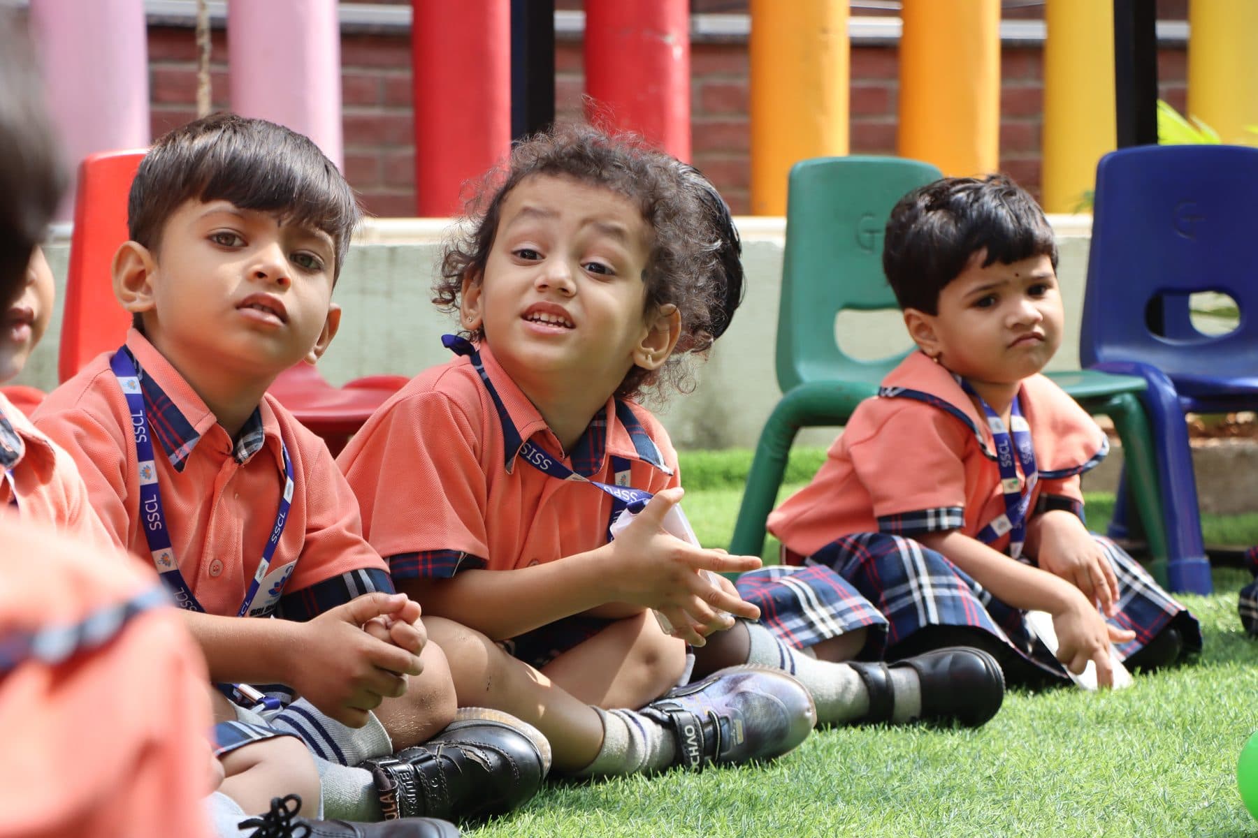Children sitting on the grass carpet, one smiling at the camera