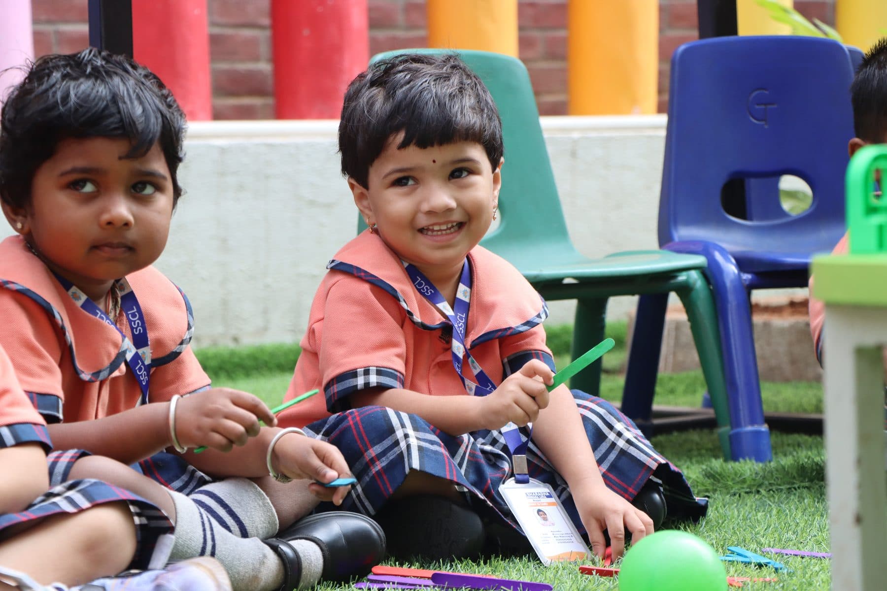 Two little ones sitting on the grass beside a green ball