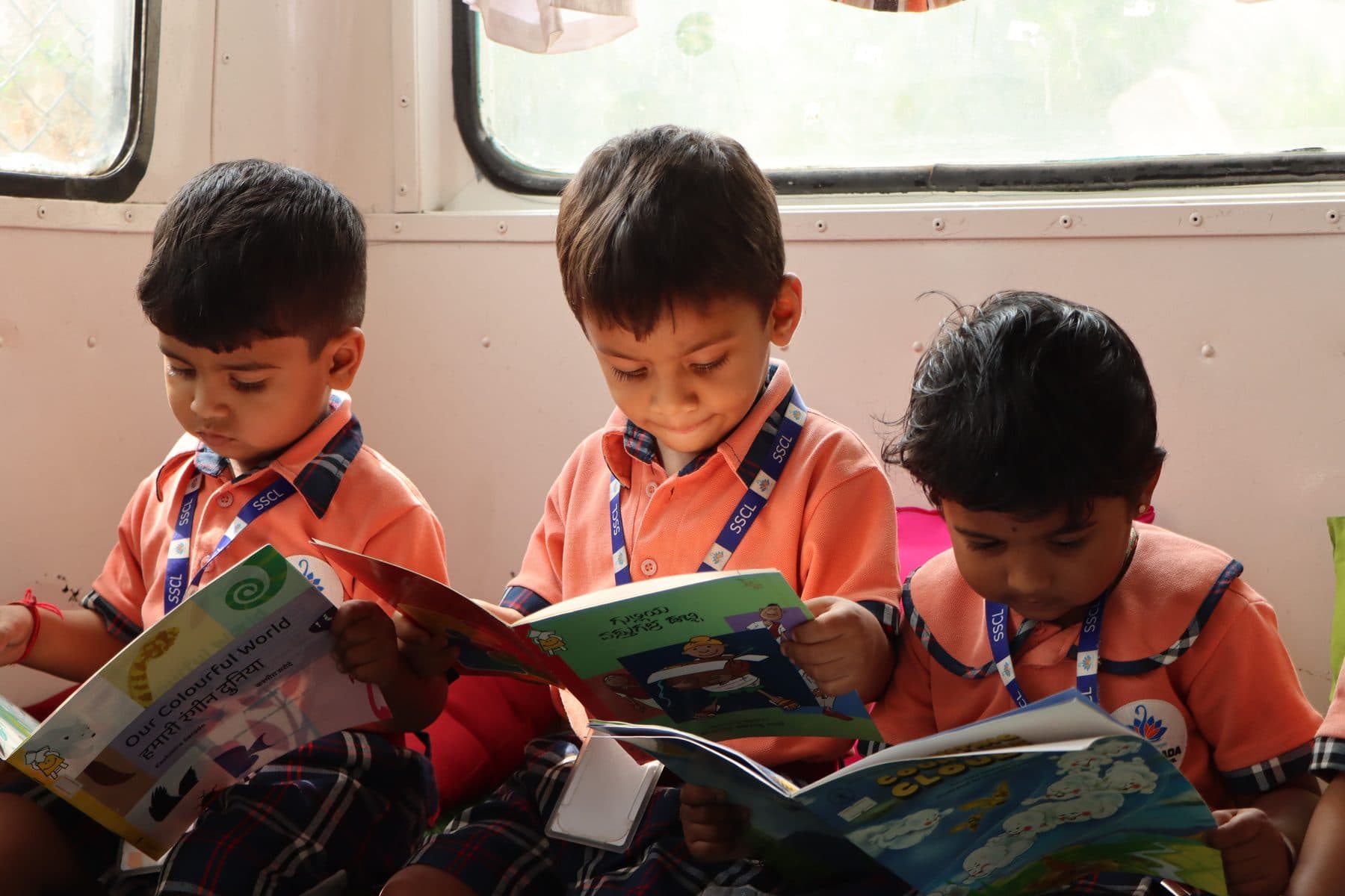 Three boys reading picture books together in the library bus