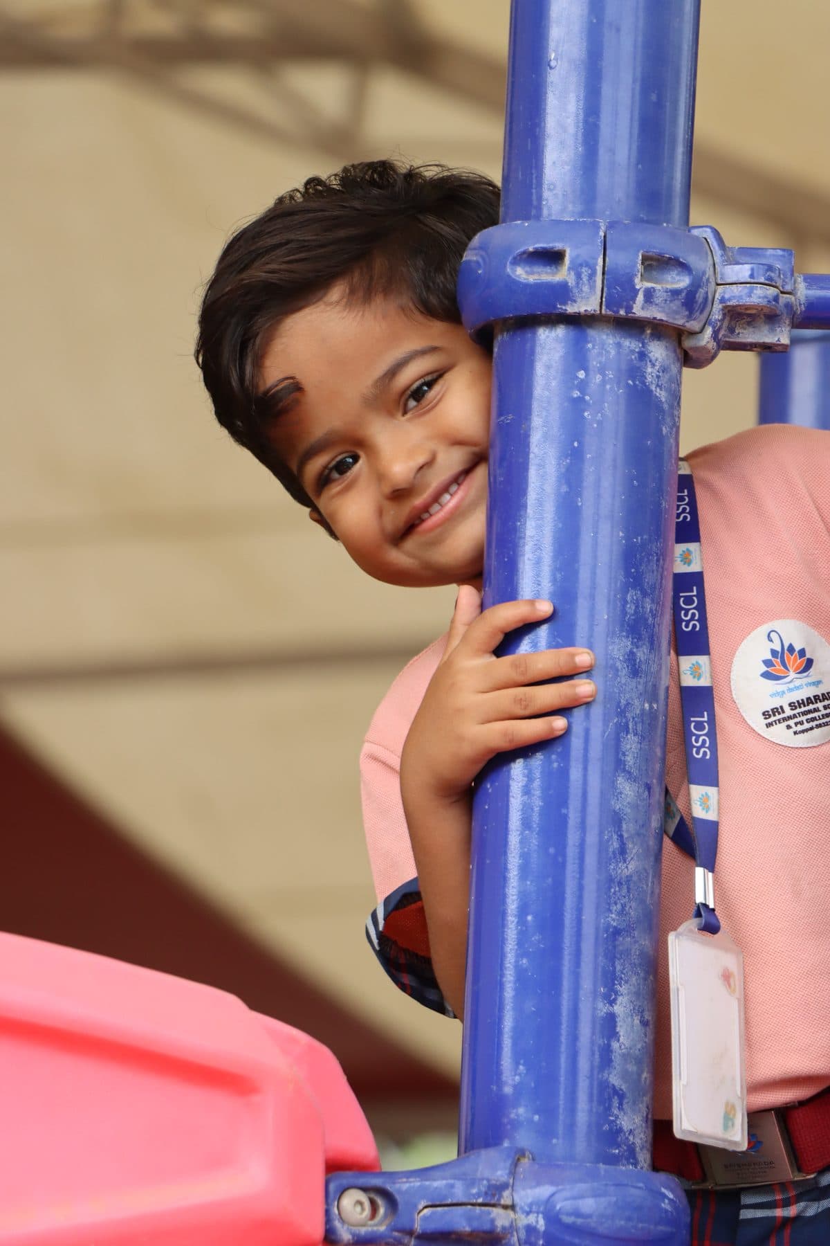 A boy hiding behind a blue pole and grinning